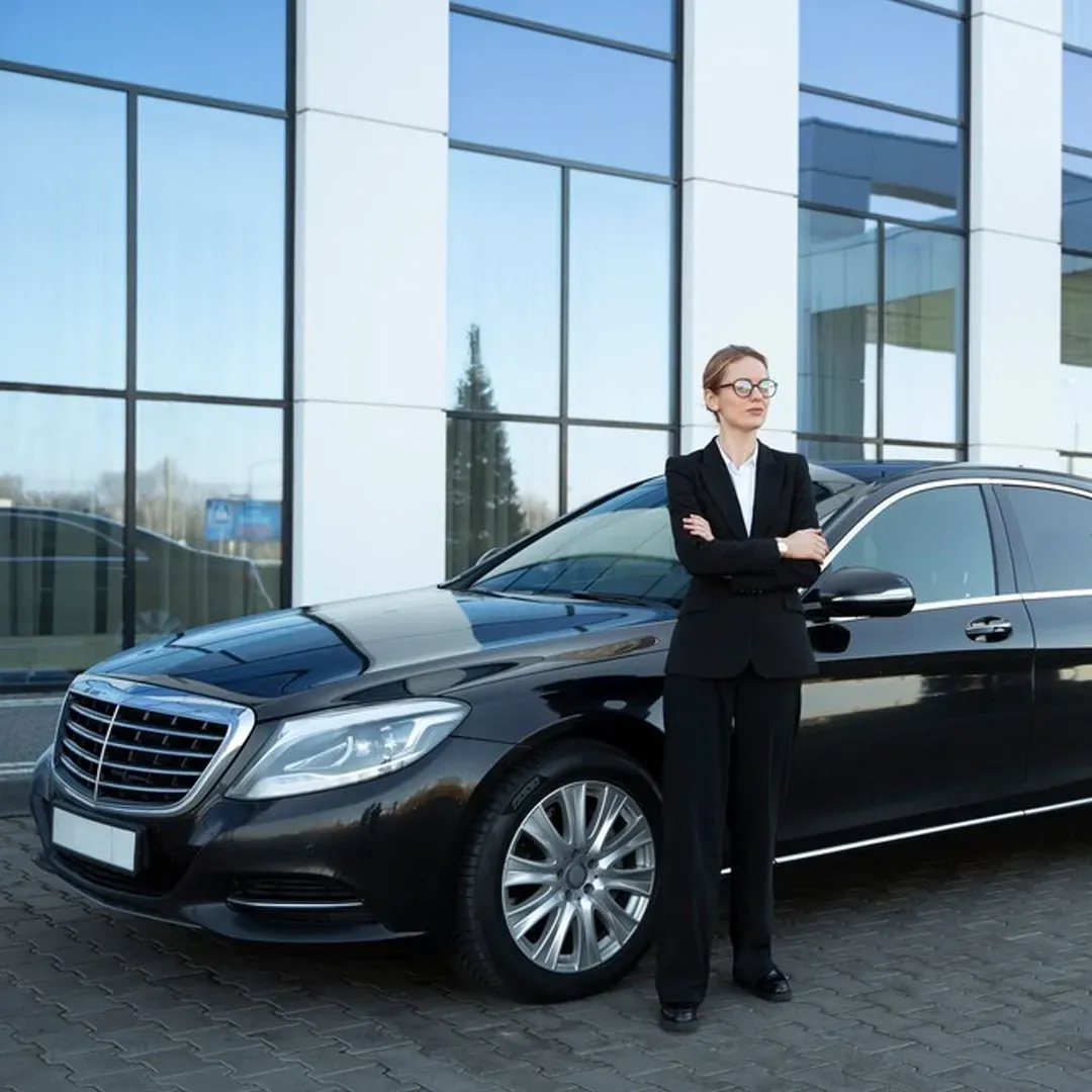 Woman in a suit standing next to a black sedan in front of a modern building.