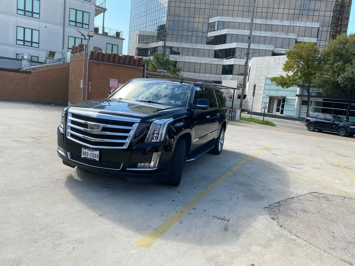 Black Cadillac SUV parked in a lot with city buildings in the background.