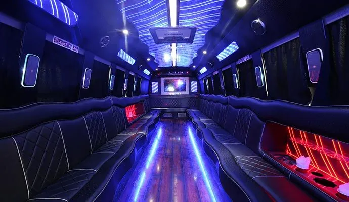 Interior of a party bus with black leather seating, neon blue and red lights, and a wooden floor.
