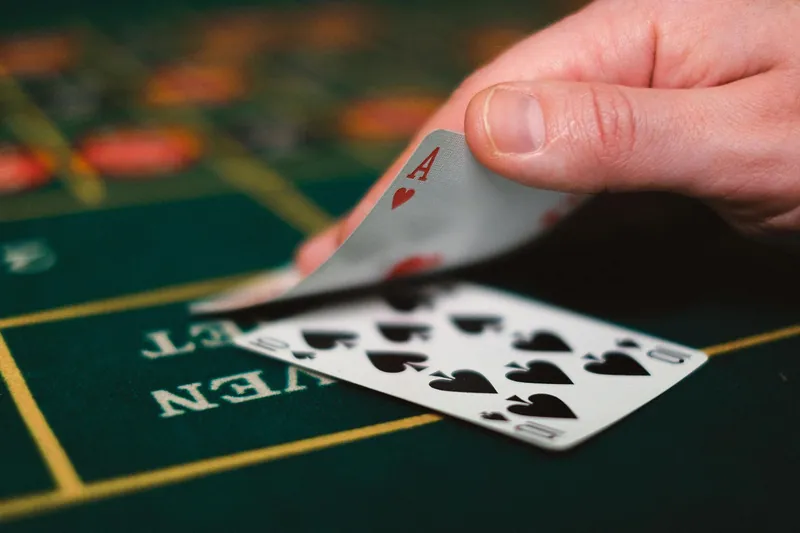 Hand holding playing cards on a green table, revealing an Ace and a ten of spades.